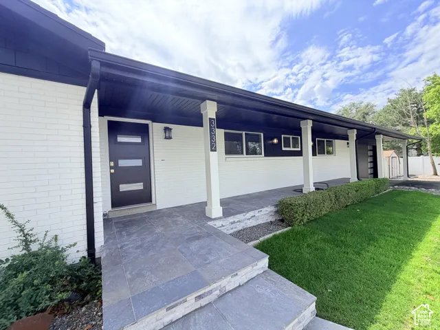 White brick exterior with black trim, a dark entry door with frosted glass inserts, and a covered porch with white columns