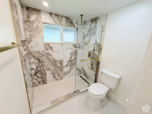Shower with full-height marble-style tile surround, glass enclosure with gold-tone accents, and a built-in shower niche