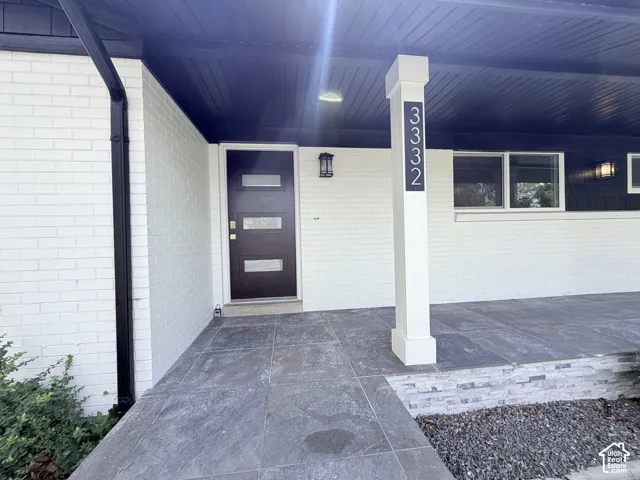 White brick exterior with a dark wood-finish entry door, multiple windows, and a covered porch