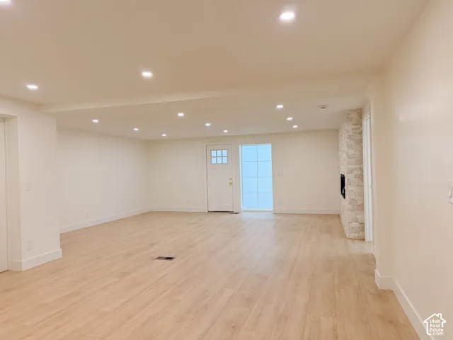 Recessed lighting, light wood-finish flooring, white baseboards, a door with window panes, and a stacked stone fireplace surround