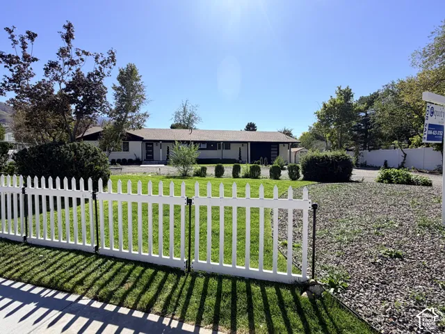 White picket fence, manicured lawn, established shrubbery, mature trees, and a gravel driveway