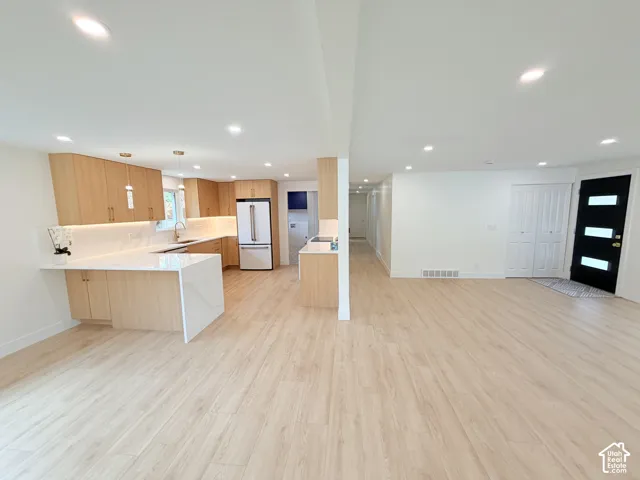 Open-concept living space with light wood-finish flooring, recessed lighting, a kitchen island with a waterfall countertop, and light wood cabinetry