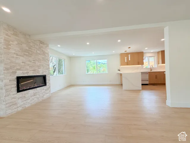 Recessed lighting, wood-finish flooring, stone-clad fireplace, kitchen island with waterfall countertop, and wood cabinetry