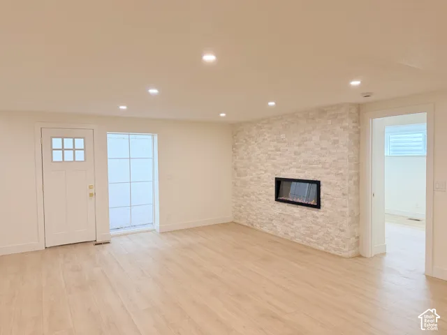 Spacious room featuring wood-finish flooring, recessed lighting, a fireplace with a stacked stone surround, a white paneled door with glass inserts, and a large multi-pane window