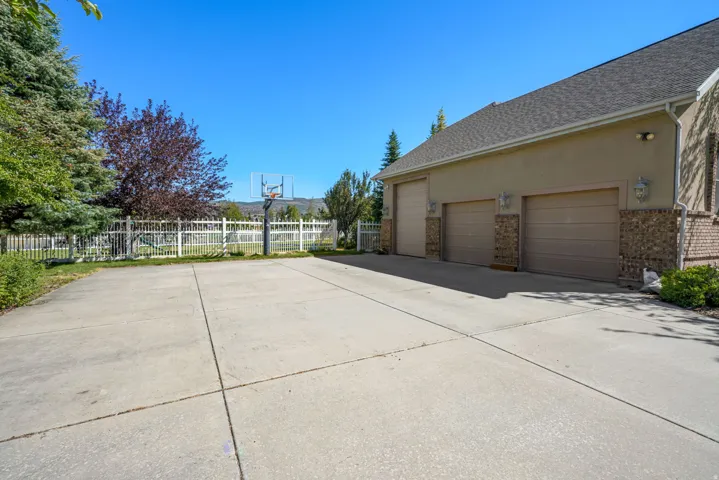 Three-car garage with individual doors, stone accents, exterior wall sconces, and an expansive concrete driveway