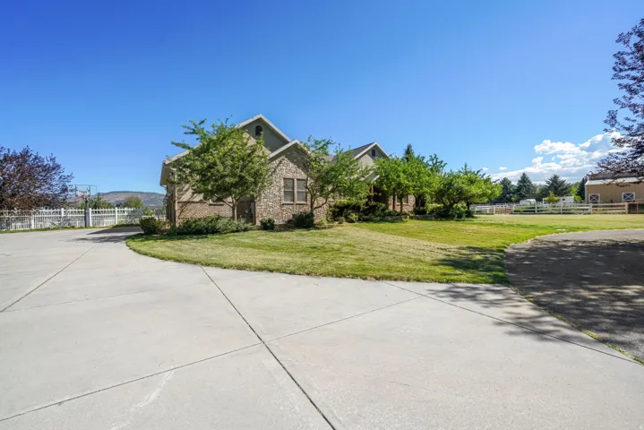 Concrete driveway leading to a stone-clad home, featuring gabled rooflines, mature landscaping, and an expansive lawn