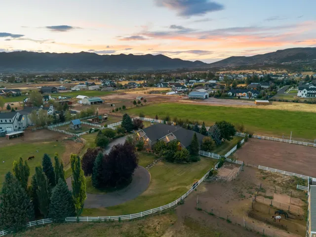 Expansive property featuring a circular driveway, mature landscaping, white perimeter fencing, and a dedicated equestrian area