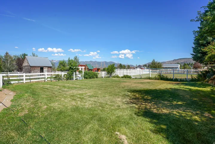 Expansive grassy yard with white picket fencing, established trees, and mountainous terrain in the distance