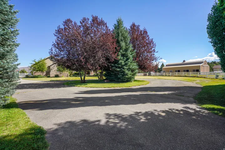 Paved circular driveway with a central landscaped island featuring mature trees, a detached barn structure, and a brick-sided residence