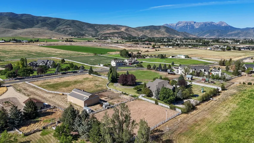 Expansive property featuring a large barn, fenced paddocks, surrounding agricultural fields, and distant mountain ranges