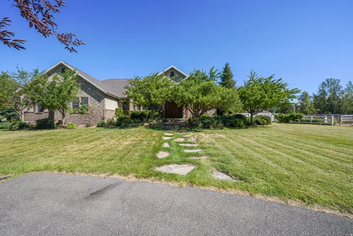 Stately brick residence set on expansive grounds featuring a manicured lawn, mature shade trees, and white fencing