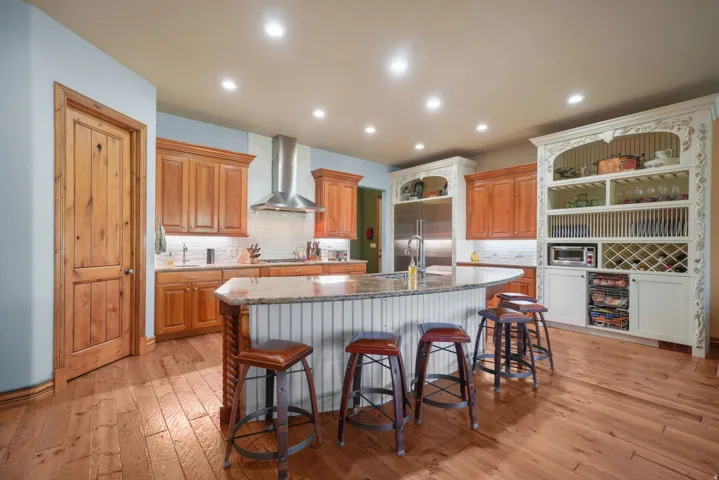 Spacious kitchen featuring wood-finish flooring, a substantial island with seating, wood cabinetry, stainless steel appliances, and built-in display shelving