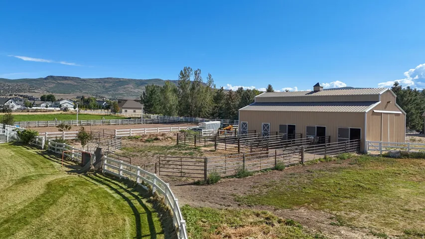 Barn structure with multiple stalls, adjacent fenced paddocks, and a large riding arena