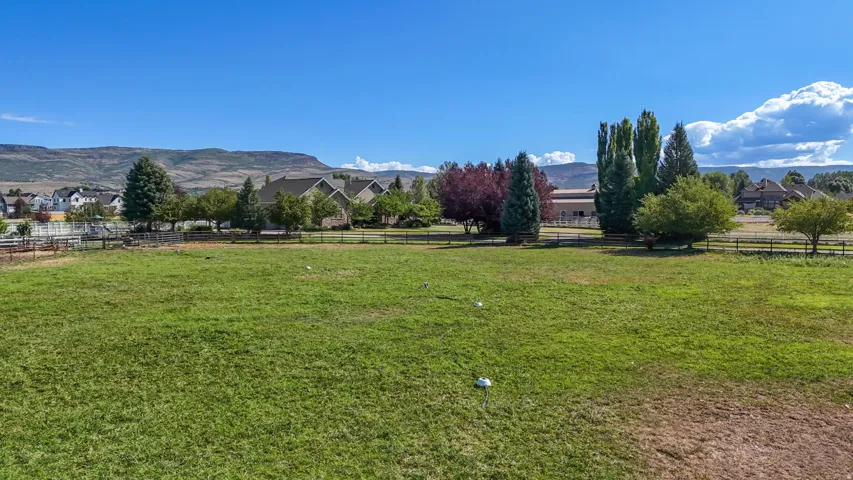 Expansive grassy field with perimeter fencing, mature trees, and distant mountain backdrop