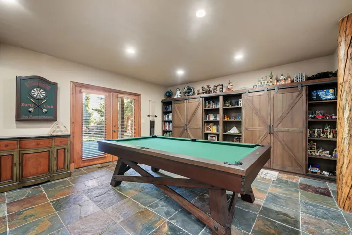 Natural stone flooring, recessed lighting, built-in shelving with sliding barn doors, and French doors