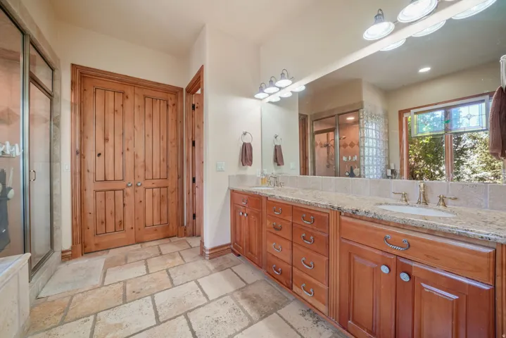Dual-sink vanity with a light-toned countertop, wood cabinetry, and a large mirror
