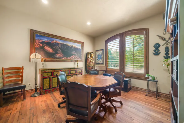 Hardwood flooring and recessed lighting illuminate this versatile space, featuring arched window frames with wood shutters and a built-in shelving unit