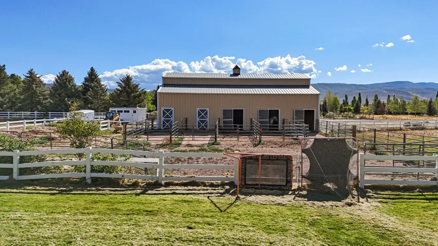 Barn structure with a metal roof and cupola, featuring multiple stalls with half-doors, and surrounding fenced areas