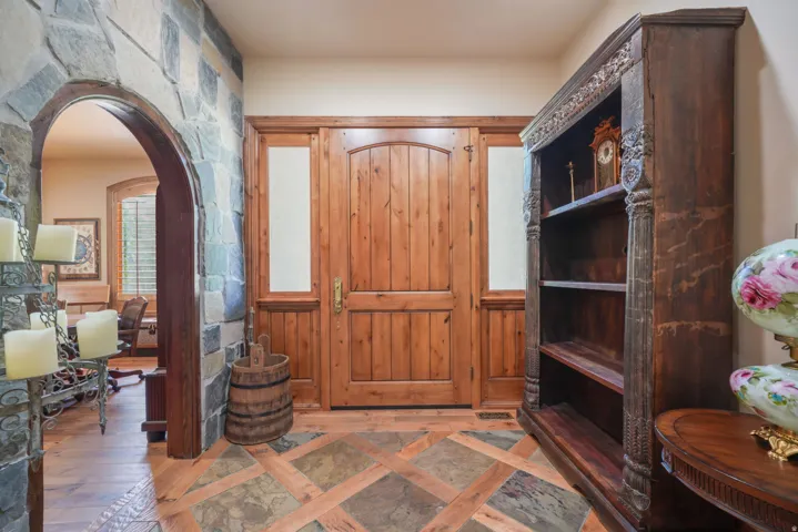 Solid wood entry door with sidelights, stone and wood-finish flooring, and a stone archway
