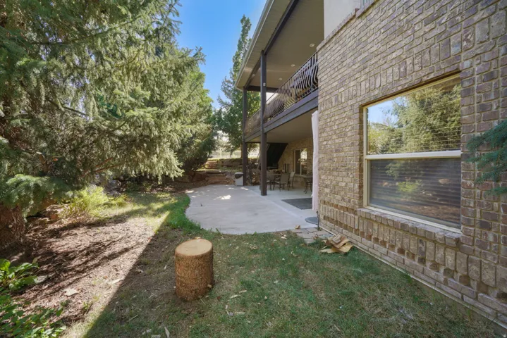 Brick exterior with a ground-level patio, upper-level balcony, and mature evergreen trees