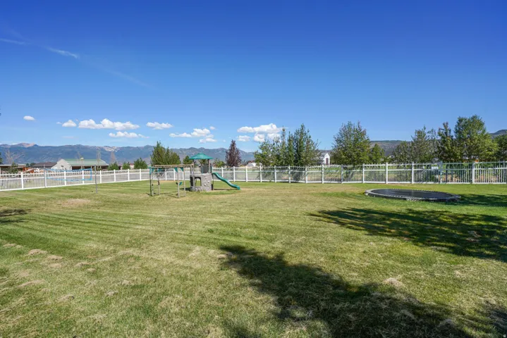 Expansive grassy yard with white fencing, mature trees, and mountainous backdrop