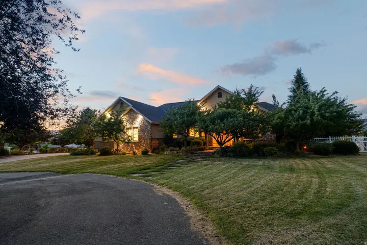 Stone façade residence with a dark shingle roof, established landscaping, and a paved driveway