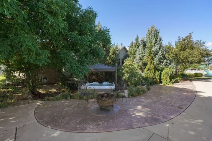 Stamped concrete patio with a fire pit, a hot tub under a metal gazebo, and mature landscaping