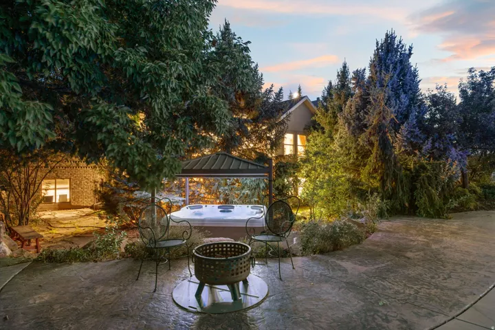 Stamped concrete patio, covered hot tub, fire pit, mature trees, and exterior lighting