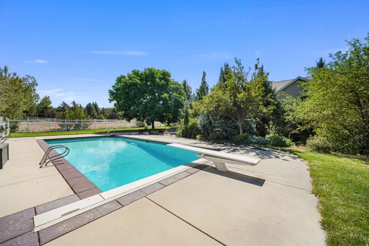 Outdoor swimming pool featuring a diving board, surrounding concrete patio, and lush perimeter landscaping