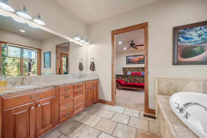 Dual vanity with granite countertops, wood cabinetry, and a full-width mirror