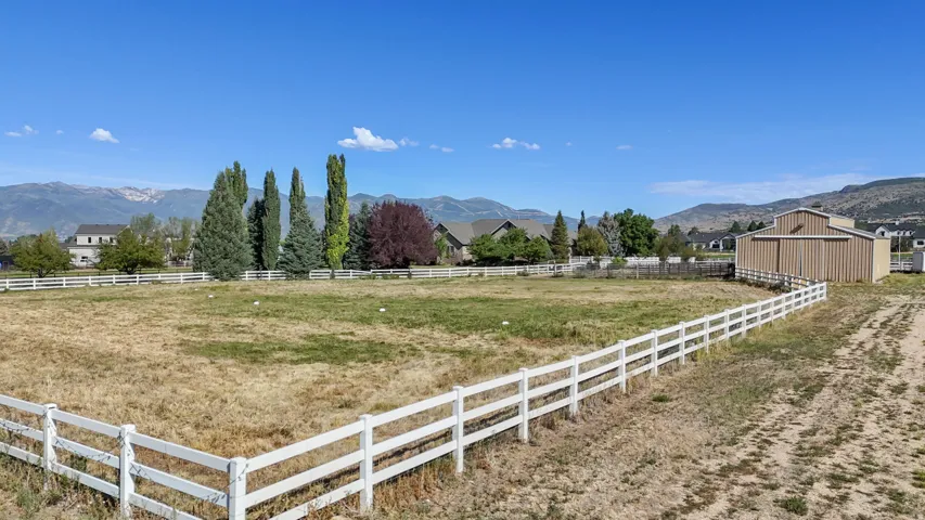 Expansive lot featuring a white fence boundary, established trees, a barn structure, and mountain scenery