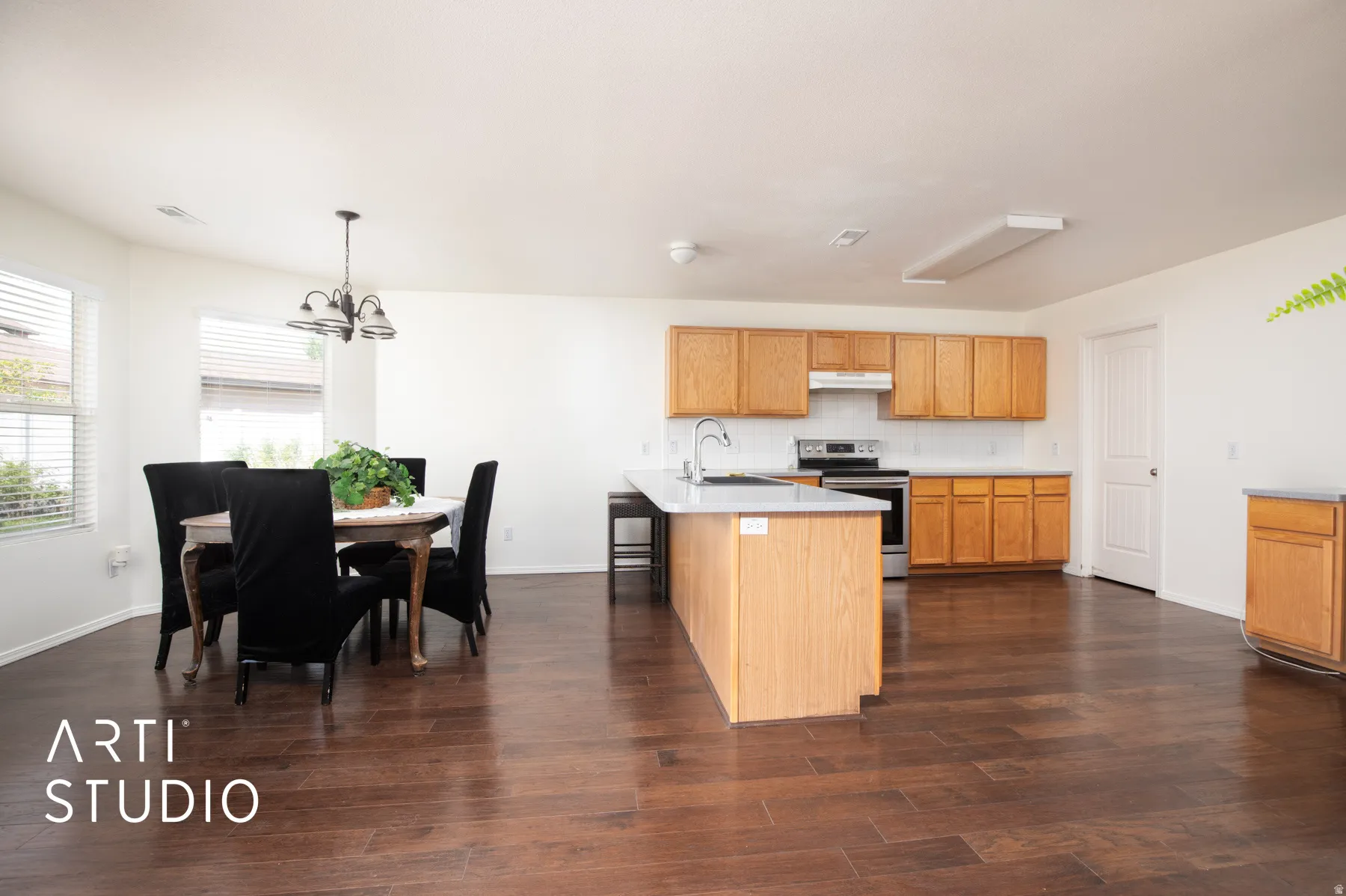 Wood-finish flooring throughout, light wood cabinetry, kitchen island with sink, stainless steel range, and tile backsplash