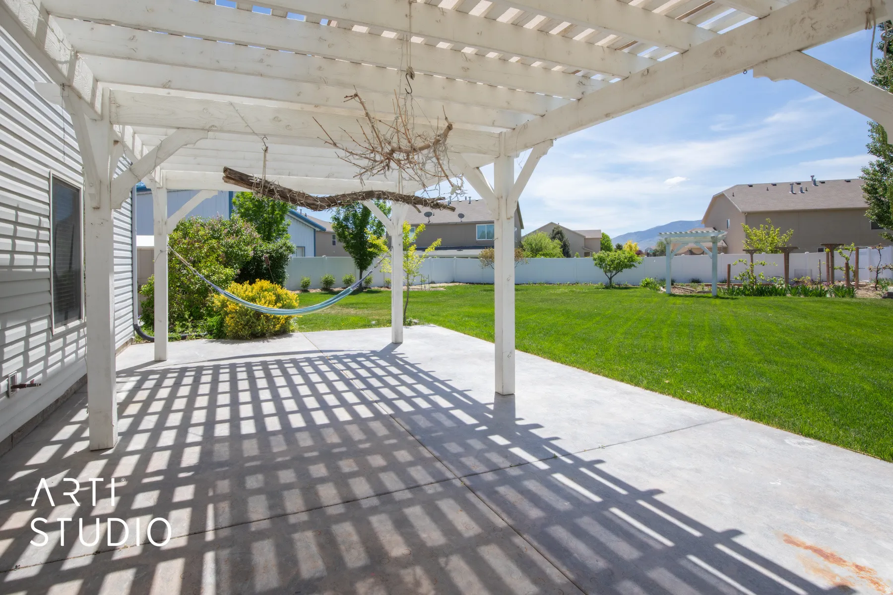 Expansive backyard with a white pergola, concrete patio, and a vast lawn area