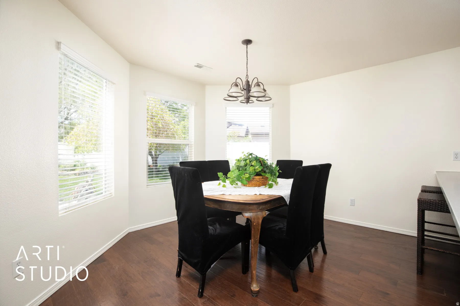 Wood-finish flooring, multiple windows with blinds, a ceiling-mounted chandelier, and white walls