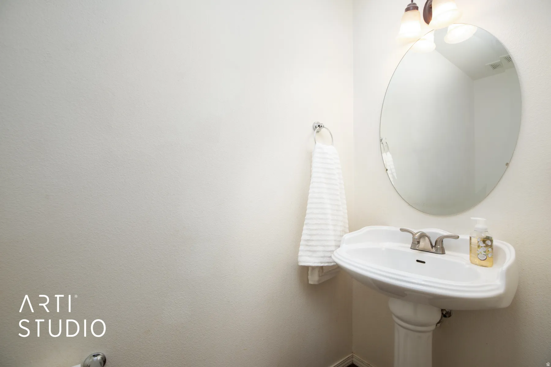 Pedestal sink with a brushed nickel faucet, an oval mirror, and a wall-mounted light fixture