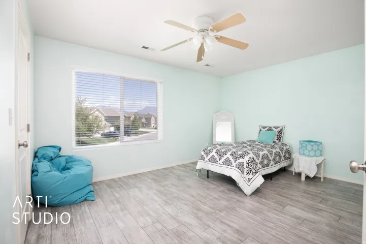 Wood-finish flooring, light-colored walls, window with horizontal blinds, and a ceiling fan with integrated lighting