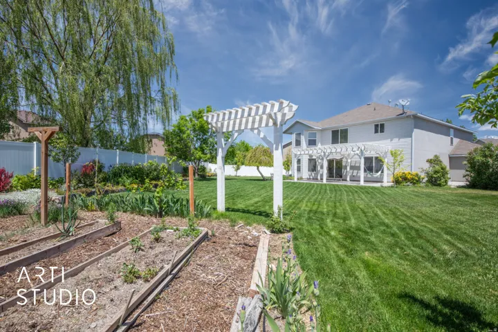 Expansive backyard featuring a manicured lawn, a white pergola-covered patio, raised garden beds, and a white privacy fence
