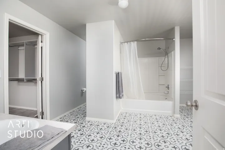 Bathroom featuring patterned floor tiling, a white bathtub with a shower, and an integrated vanity sink with a light-colored countertop