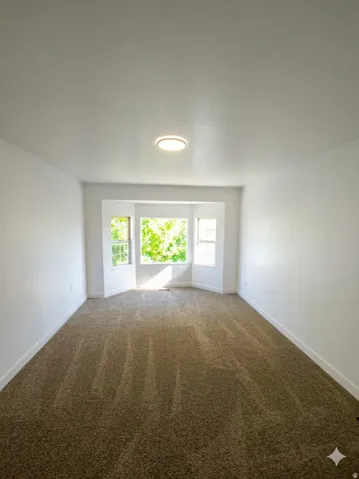 Recessed bay window with multiple panes, neutral-toned carpeting, and a flush-mount ceiling light fixture