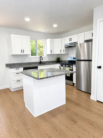 Kitchen featuring wood-finish flooring, white cabinetry, granite countertops, an island, and stainless steel appliances