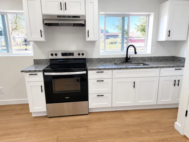 Kitchen featuring wood-finish flooring, white cabinetry with matte black hardware, speckled countertops, a stainless steel range, and a black gooseneck faucet