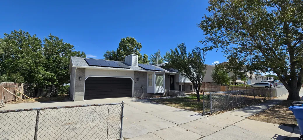 Single-story residence featuring solar panels, an integrated garage with a dark panel door, and a paved driveway