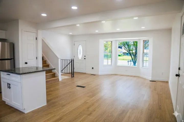 Light wood-finish flooring throughout, recessed lighting, white cabinetry, dark stone-finish countertop, and a bay window