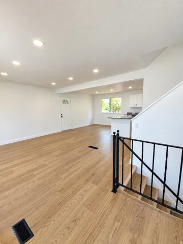 Open-concept living area with wood-finish flooring, recessed lighting, and a white paneled entry door with an arched glass insert