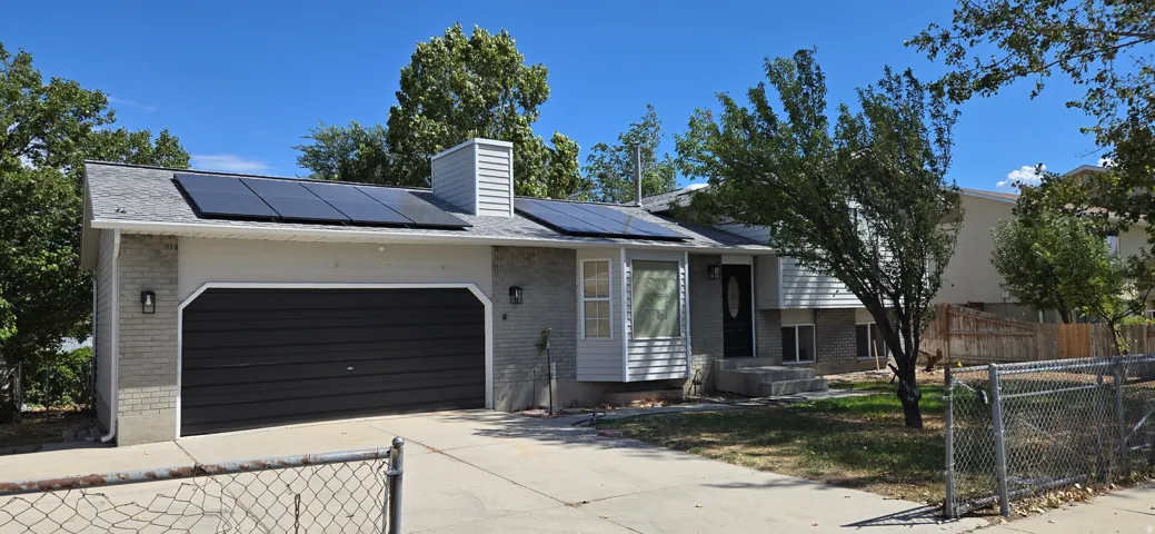 Exterior featuring solar panels, an attached garage with a dark panel door, and gray siding accents