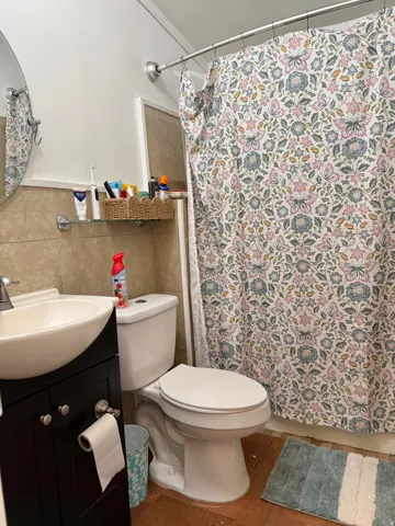 Wall-mounted circular mirror, vessel sink with a dark wood-finish vanity, tiled walls, and a white toilet