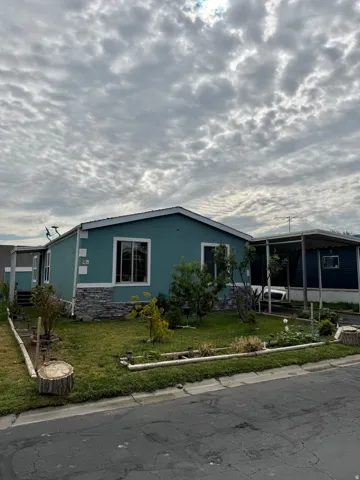 Exterior featuring blue siding, stone-look skirting, white trim windows, a covered carport, and a landscaped front yard with decorative curbing