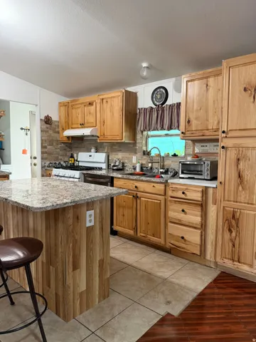 Kitchen featuring light wood cabinetry, stone-look tile backsplash, light granite-look countertops, and a central island with wood-finish paneling
