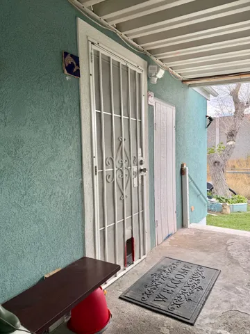 Secured entry with a metal security screen door, stucco exterior, and a covered patio area