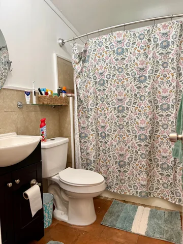 White porcelain toilet, dark wood-finish vanity with a vessel sink, and a tiled shower surround